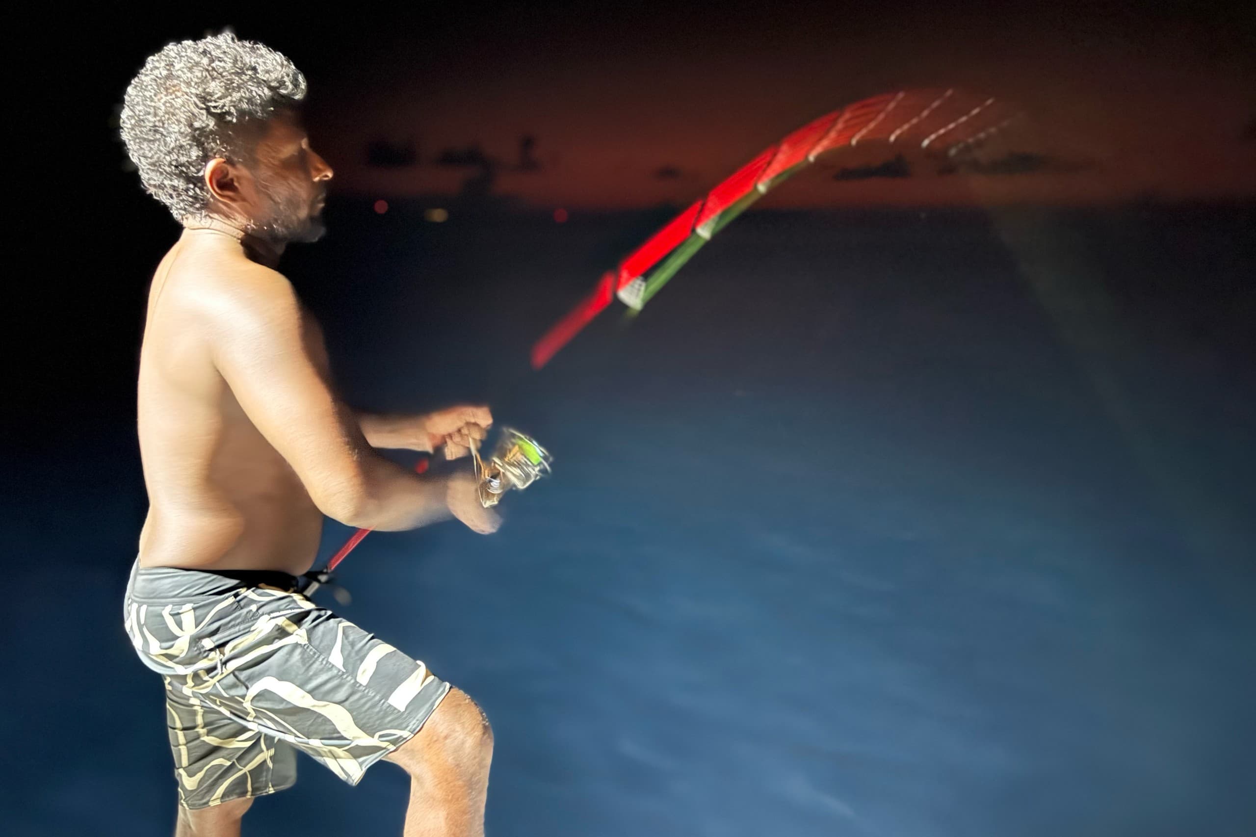 Night fishing experience in Maldives with angler casting line into the ocean under dark sky